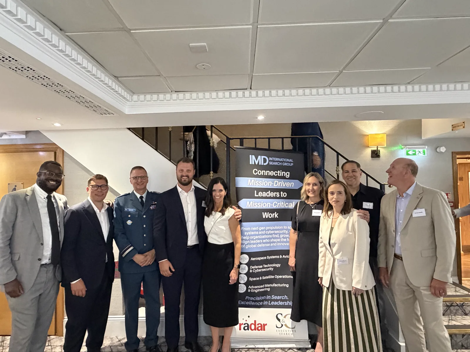 Jose J. Ruiz con socios de la Práctica Aeroespacial de IMD International Search Group frente al banner de IMD — Connecting Mission-Driven Leaders to Mission-Critical Work — en el Farnborough International Airshow, Día 3, 22 de julio de 2026.